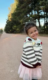 Sweater tejido a mano en lana merino, con cuello redondo y diseño con rayas horizontales en tonos crudo y marrón. Presenta bordados de animales y flores en la parte superior. Tiene puños y ruedo acanalados en color bordó.