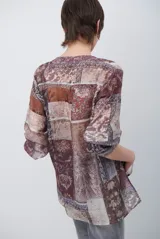 Camisa de corte recto con cuello mao y cierre frontal parcial de botones. Presenta un diseño estampado tipo patchwork con motivos florales y geométricos en tonos tierra, marrones y beige. Posee mangas tres cuartos con puños simples.