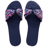 Sandalias tipo chinela Havaianas con base de goma azul marino y tira superior de tela con nudo central y estampado floral en tonos rosados y blancos.