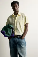 Camisa de corte regular fit color amarillo con rayas verticales blancas, cuello solapa, manga corta, bolsillo de parche en el pecho y cierre frontal con botones.
