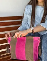 Cartera tipo sobre de gamuza con diseño de franjas verticales en tonos marrón y fucsia, con borlas colgantes a los laterales.