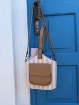 Bolso matero estructurado con diseño a rayas verticales en tonos beige y blanco, cuenta con un bolsillo frontal externo en cuero sintético color tostado, asa de mano corta y correa larga ajustable y desmontable.