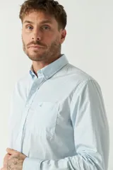 Camisa celeste de manga larga con logo bordado y bolsillo en el pecho.