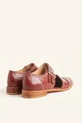 Zapato tipo oxford abierto en los laterales, confeccionado en cuero vacuno negro. Presenta doble tira con hebillas metálicas en el empeine y detalle de tachas plateadas en el contorno del talón y la puntera.