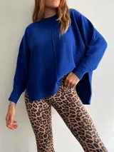 Sweater oversize de tejido liviano, color beige, con cuello redondo, mangas largas con puños acanalados y tajos laterales. Presenta una costura vertical decorativa en el frente y un diseño más largo en la parte posterior.