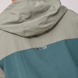 Campera cortavientos Rusty modelo Aidan, con diseño de bloques de color en tonos verde y gris. Presenta capucha, cierre frontal completo, puños elásticos y bolsillos laterales.