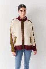 Campera de tejido de punto con cierre frontal, cuello alto y bolsillos laterales. Presenta un diseño tricolor en tonos crema, bordó y verde oliva, con detalles de costuras decorativas y paneles laterales con textura trenzada.
