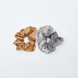 Pack de dos coleteros tipo scrunchie, uno de color beige liso con acabado satinado y otro con estampado de piel de serpiente en tonos blanco y negro.