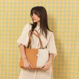 Cartera tipo tote de cuero sintético con diseño combinado en tono gris y blanco, textura granulada, asas largas para el hombro y cierre superior.