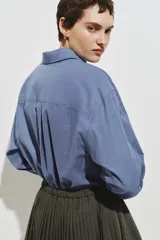 Camisa de corte oversized confeccionada en popelina de algodón con diseño de microcuadros. Presenta cuello clásico, bolsillo de parche en el pecho, cierre frontal con botones, hombros caídos y mangas largas con puños abotonados. Incluye canesú con pliegue en la espalda y bajo recto con aberturas laterales redondeadas.
