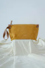 Sobre de cuero agamuzado color mostaza, con cierre de cremallera y logo grabado en el frente.