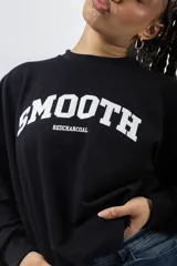Buzo color crema con estampado frontal que dice "SMOOTH" en marrón y "REDCHARCOAL" debajo. Tiene cuello redondo y mangas largas.