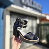 Sandalias de cuero color suela y beige, con plataforma de madera, taco ancho y doble tira con hebillas metálicas en el tobillo. Cuentan con cierre trasero.
