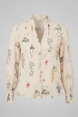 Camisa color arena con estampado botánico de flores silvestres, cuello mao con volados, escote en V y cierre frontal con botones. Las mangas son largas con hombros ligeramente fruncidos y puños elastizados con acabado de volados.