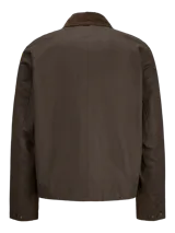 Campera de estilo worker color marrón, con cuello camisero de pana, cierre frontal con cremallera y bolsillos frontales con solapa y broches a presión. Presenta un acabado recubierto que le otorga una textura sutilmente brillante y resistente.