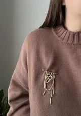 Set de accesorios compuesto por un sobre organizador de gamuza color marrón, un collar de cadena dorada, dos pares de caravanas colgantes y un prendedor, todos en metal dorado.