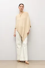 Capa tejida en hilo de lurex color beige, con cuello bote y diseño asimétrico de corte fluido.