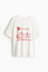 Remera oversized de punto de algodón color blanco, con cuello redondo ribeteado y moldería de hombros caídos. Cuenta con estampa frontal en color rojo con motivo de playa y la inscripción "WHERE THE MOUNTAINS MEET THE SEA" y "SANTA BARBARA, CALIF.".
