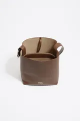 Bolso de hombro tipo cubo de estructura rígida, color marrón oscuro, confeccionado en piel vacuna. Posee asa regulable con hebilla metálica y cierre de cordón en la parte superior. Lleva el logo metálico de Bimba y Lola en la parte frontal inferior.