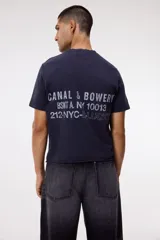 Remera de algodón color gris oscuro con cuello redondo y estampado pequeño en el pecho con texto en color blanco.