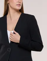Blazer de sastrería color beige, sin solapas, con cuello en V profundo y cierre frontal de un único botón circular metálico en contraste.