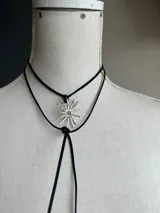 Colgante con dije en forma de sol con rayos, hecho a mano en alpaca, con cordón de gamuza marrón.