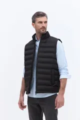 Chaleco puffer negro con diseño acolchado horizontal, cuello alto y cierre frontal. Presenta un bolsillo lateral con detalle de marca grabado.