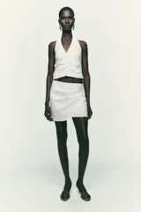 Top negro con cuello halter, escote pico y espalda descubierta. Presenta detalle de frunces laterales y cierre frontal con botones.