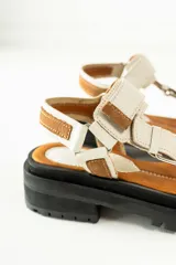 Sandalias negras de estilo chunky con plataforma dentada. Presentan tiras ajustables con cierre de velcro y hebillas metálicas, combinando texturas de cuero granulado y detalles en charol.