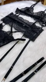 Conjunto de lencería de cuatro piezas en encaje negro. Incluye bralette con breteles regulables, tanga con tiras dobles ajustables en la cintura, portaligas con enganches desmontables y ligas para las piernas.