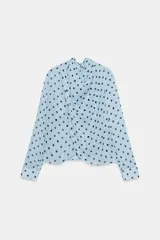 Camisa de manga larga con cuello fluido y diseño cruzado en el frente. Confeccionada en tejido semitransparente de color celeste con estampado de lunares negros. Presenta bajo asimétrico y cierre en la espalda con botones forrados.