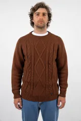 Buzo de lana merino color marrón con diseño de tejido trenzado en el frente y cuello redondo acanalado. Presenta puños y ruedo elásticos, con una pequeña etiqueta decorativa en la parte inferior.