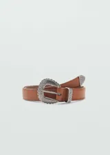Cinturón de estilo western en color marrón, confeccionado en material sintético con acabado liso. Presenta una hebilla metálica plateada con detalles grabados en relieve y una puntera metálica a juego.