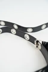 Cartera negra de hombro con flecos laterales, cierre de cremallera y correa ajustable con detalles metálicos.