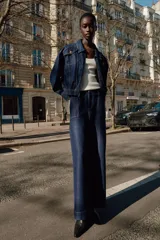 Chaqueta estilo bomber de Zara confeccionada en tejido denim azul oscuro. Presenta cuello solapa, cierre frontal con cremallera, bolsillos delanteros con solapa y bajo elástico que le otorga un ajuste ceñido en la cintura.