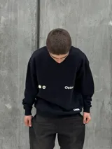 Buzo negro de corte holgado con cuello redondo y puños y bajo acanalados. Estampado frontal con un sol y la palabra "Osten" en blanco.