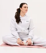 Buzo deportivo con capucha gris melange, con cordones ajustables blancos, bolsillo tipo canguro y pequeño estampado tipográfico en el pecho con la inscripción 'Wellness Club'.