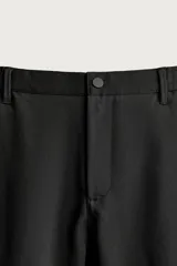 Pantalón de corte slim fit y color negro, confeccionado en tejido elástico. Cuenta con cintura elástica, trabillas, bolsillos frontales y cierre con cremallera y botón.