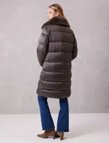 Campera puffer larga de acabado satinado en tono beige. Presenta un diseño capitoneado horizontal, cierre frontal bidireccional y un amplio cuello envolvente revestido en piel sintética. Incluye bolsillos laterales funcionales con cierre y logo metálico en la manga.