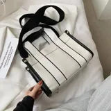Bolso tipo tote bag de lona color blanco con detalles y tiras de cuero sintético color marrón caramelo. Posee asas cortas y una correa ajustable y desmontable para llevar al hombro o cruzado.