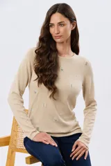 Buzo tejido de algodón color beige, de manga larga, con cuello redondo y delicados motivos bordados distribuidos en la prenda.