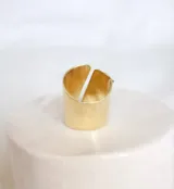 Anillo dorado con diseño abierto y dos piedras incrustadas, una blanca y otra verde.