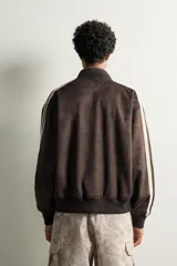 Cazadora relaxed fit de tejido efecto ante color marrón oscuro, con cuello subido y cierre frontal de cremallera. Presenta mangas largas con bandas blancas a contraste en los hombros, bolsillos laterales de vivo, y bordados en hilo blanco en el pecho.