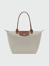Mochila de diseño minimalista en color beige, con solapa y asa superior en cuero marrón texturizado. Cuenta con correas ajustables en color marrón y cierre principal.