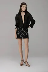 Camisa de organza negra con diseño semitransparente, cuello camisero clásico, mangas largas con puños estructurados y cierre frontal con botones.