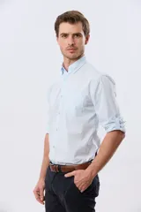 Camisa celeste de manga larga confeccionada en algodón, con cuello camisero, cierre frontal de botones, bolsillo en el pecho y diseño de cuadros sutiles.