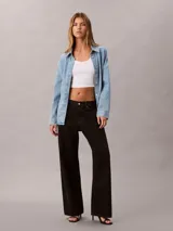 Camisa de denim de corte holgado, con cuello en punta, mangas largas y cierre frontal con botones. Presenta un diseño clásico con acabado lavado y monograma bordado en el pecho.