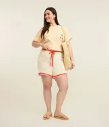 Blusa boxy color amarillo claro con diseño de rayas sutiles, cuello redondo y mangas cortas con vuelta. Presenta un delicado bordado artesanal de frutos de cajú en la parte frontal inferior.