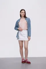 Sobrecamisa celeste de denim con cuello camisero, cierre frontal con botones a presión, dos bolsillos con solapa en el pecho y mangas largas con puños abotonados.