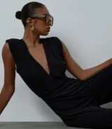 Mono largo de microfibra color negro, con escote en V profundo tipo cruzado, hombreras estructuradas y diseño sin mangas con breteles anchos. Presenta una cintura ajustada y pantalón de corte recto y amplio.